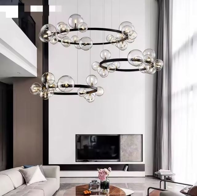 Triple suspension bulle en verre transparent, parfaite pour un salon avec haut plafond, offrant un design moderne et lumineux.