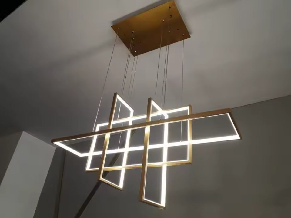Vue en contre-plongée d'une suspension LED dorée aux cadres entrecroisés, au design géométrique architectural et sculptural.