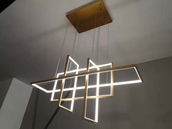 Vue en contre-plongée d'une suspension LED dorée aux cadres entrecroisés, au design géométrique architectural et sculptural.