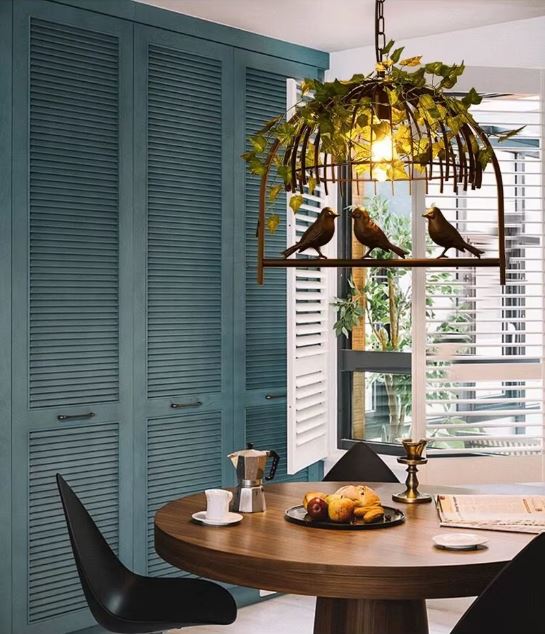 Suspension cage oiseau avec feuillage et lumière chaude, un luminaire décoratif parfait pour une cuisine au style naturel et vintage.