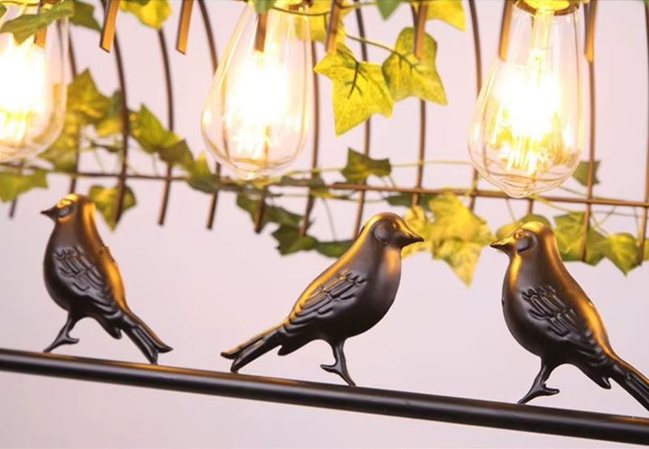 Détail d'une suspension cage oiseau en métal noir avec ampoules Edison et feuillage, un luminaire élégant au style nature et vintage.