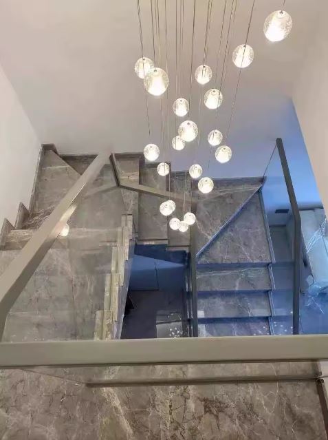 Suspension en cascade de globes en verre pour escalier en marbre, éclairage contemporain élégant et architectural.