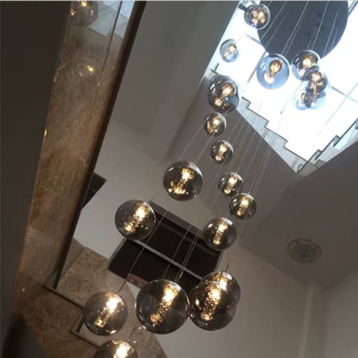 Vue en contre-plongée d’une grande suspension à globes en verre, cascade lumineuse pour plafond haut