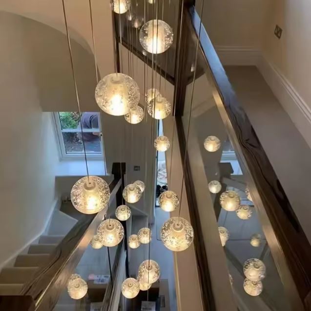 Suspension en cascade de globes en verre avec reflets miroir, éclairage sculptural pour escalier design et plafond haut.