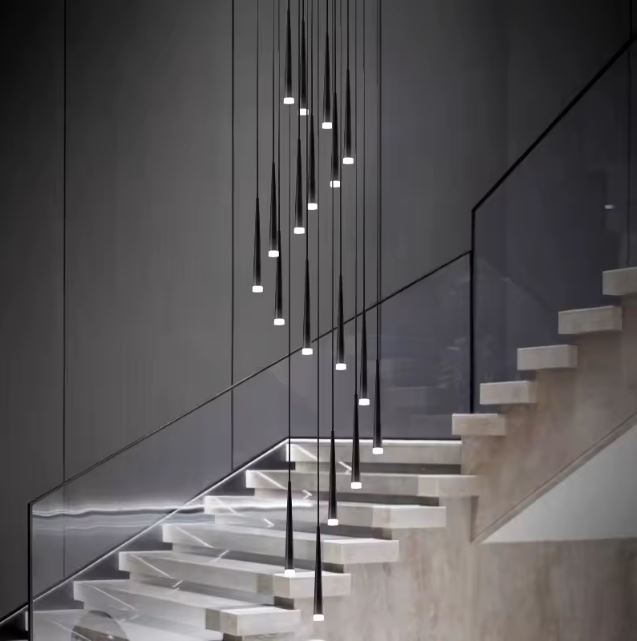 Suspension cascade grande hauteur noire illuminant un escalier en verre avec un style moderne et épuré.