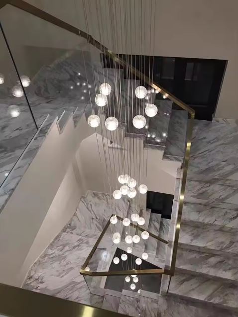 Suspension cascade de globes en verre cristallin pour escalier en marbre, ambiance luxe contemporain et éclairage architectural.