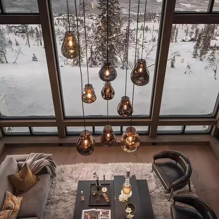 Vue plongeante sur neuf suspensions en verre soufflé aux formes organiques, éclairant un salon moderne face à un paysage enneigé.
