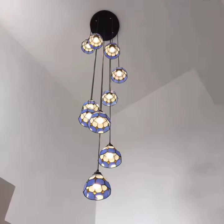 Vue en contre-plongée d’une suspension Art déco à neuf verrières bleues diffusant une lumière chaude en cascade