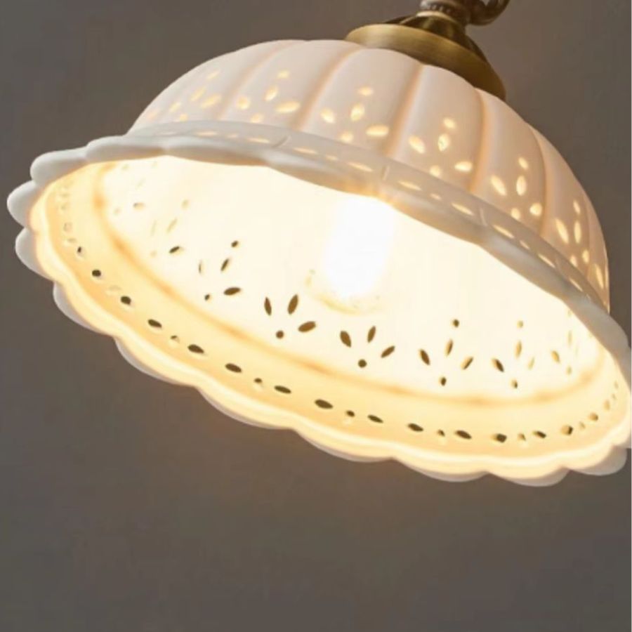 Gros plan sur une suspension en céramique blanche ajourée au charme rétro, diffusant une lumière chaleureuse