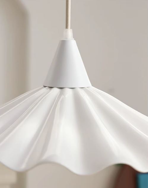 Gros plan sur suspension en céramique blanche ondulée effet jupe plissée, design scandinave épuré et lumineux.
