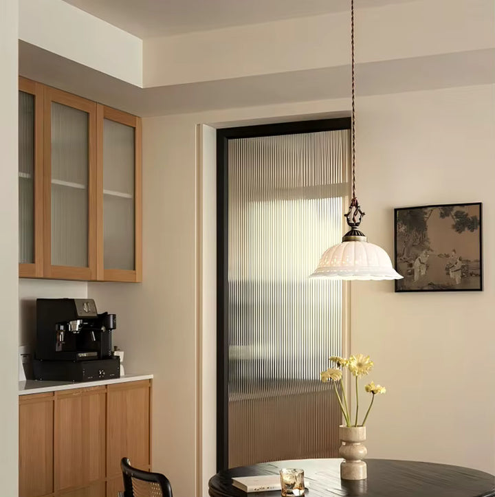 Éclairage vintage en céramique blanche suspendu au-dessus d’une table, avec détails en laiton vieilli