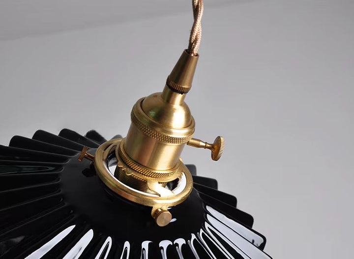 Suspension en céramique noire nervurée à collerette plissée, détail de la monture laiton évoquant un style industriel chic et contemporain élégant.