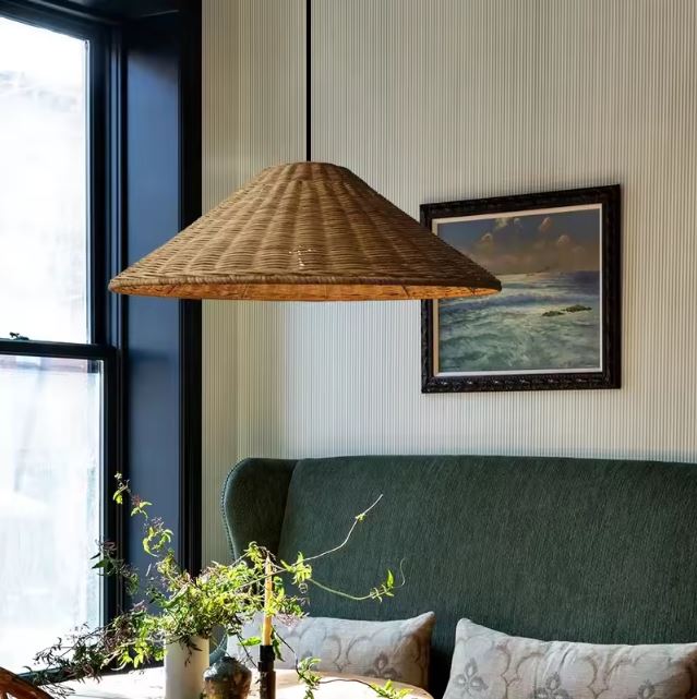 Suspension chapeau en rotin naturel illuminant un salon cosy avec un canapé vert et une ambiance chaleureuse.