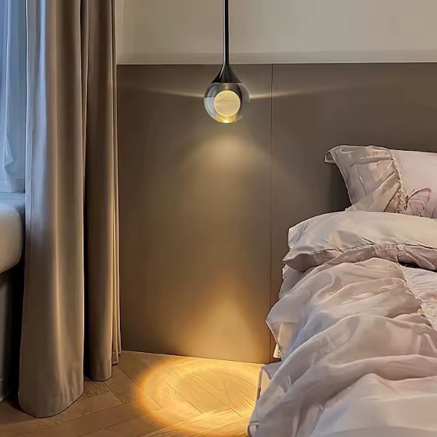 Suspension chevet en goutte de verre et métal noir, lumière d’ambiance douce pour chambre moderne au style épuré.