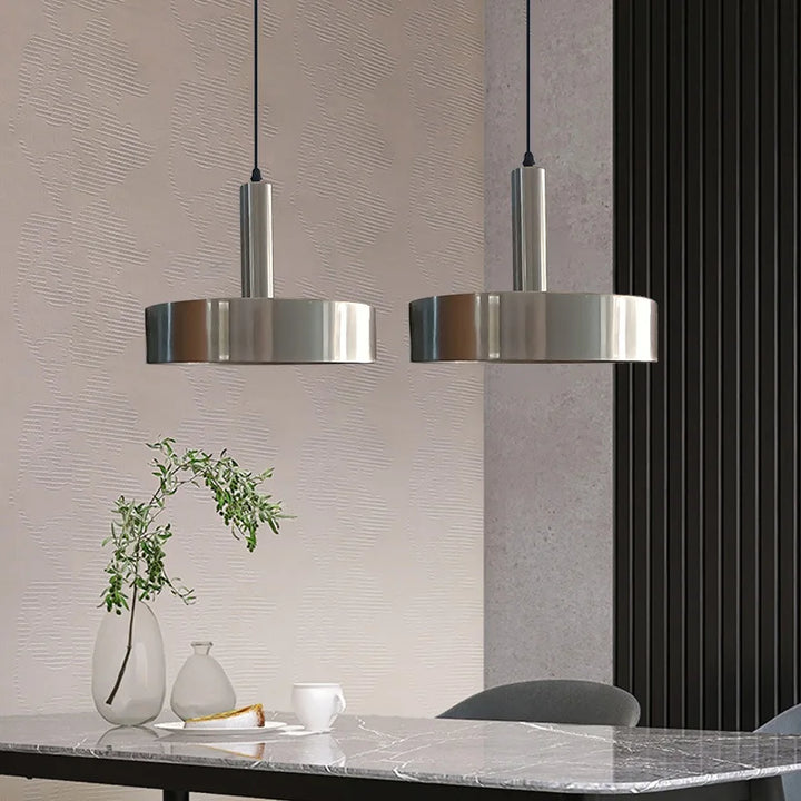 Deux suspensions cloche en métal brossé au design moderne et minimaliste suspendues au-dessus d'une table à manger.