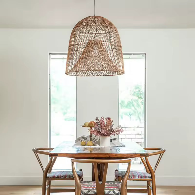 Suspension en rotin naturel à double abat-jour conique et ajouré, au-dessus d'une table en bois dans un décor bohème épuré.