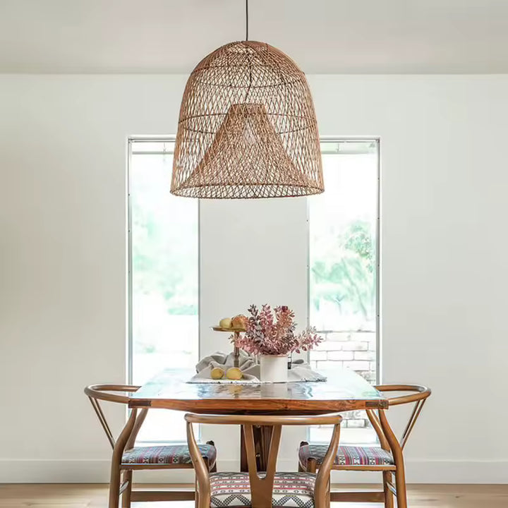 Suspension en rotin naturel à double abat-jour conique et ajouré, au-dessus d'une table en bois dans un décor bohème épuré.