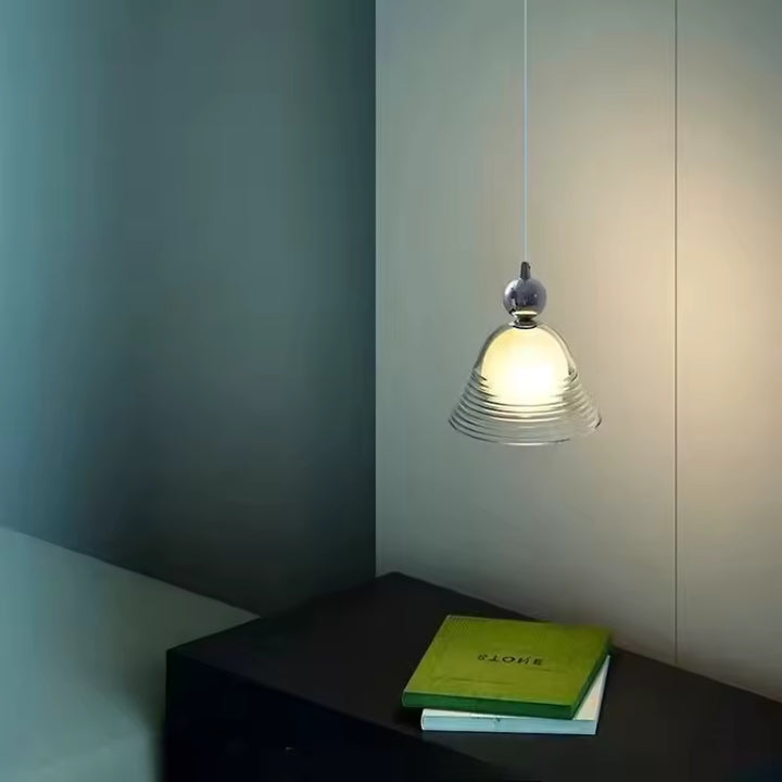 Suspension en verre soufflé strié avec globe opalin, diffusant une lumière douce près d’un chevet au style rétro