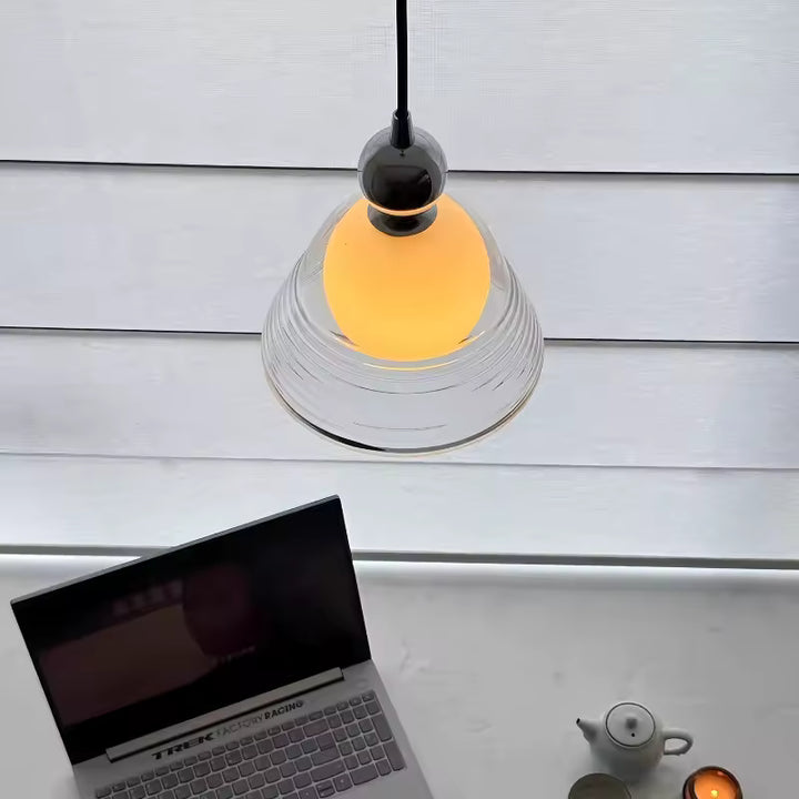 Suspension en verre soufflé strié avec globe opalin, diffusant une lumière douce au-dessus d’un bureau contemporain