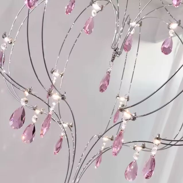 Détail d’une suspension cœur en acier inoxydable avec pampilles en cristal rose au style précieux et aérien.