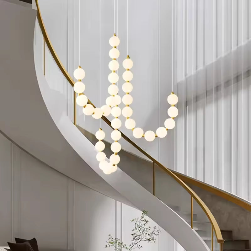 Le long d’un escalier courbe, ce lustre de globes lumineux blancs et dorés affirme un style élégant et organique