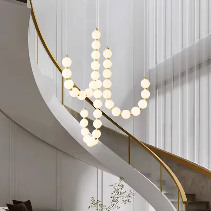 Le long d’un escalier courbe, ce lustre de globes lumineux blancs et dorés affirme un style élégant et organique
