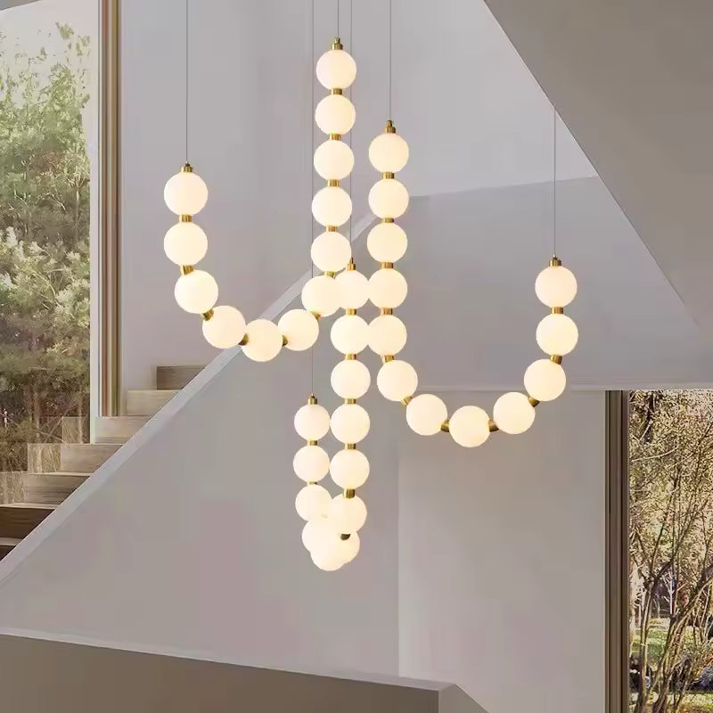 Dans une cage d’escalier, ce lustre de globes lumineux blancs et dorés crée une silhouette organique et sculpturale