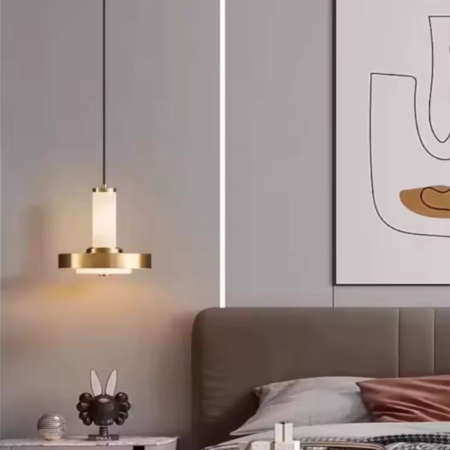 Près du lit, cette suspension à colonne et disque en métal doré diffuse une lumière douce dans une chambre contemporaine
