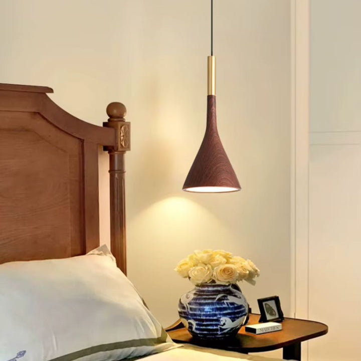Suspendu près du lit, le modèle conique effet noyer et laiton crée un éclairage chaleureux dans une chambre élégante
