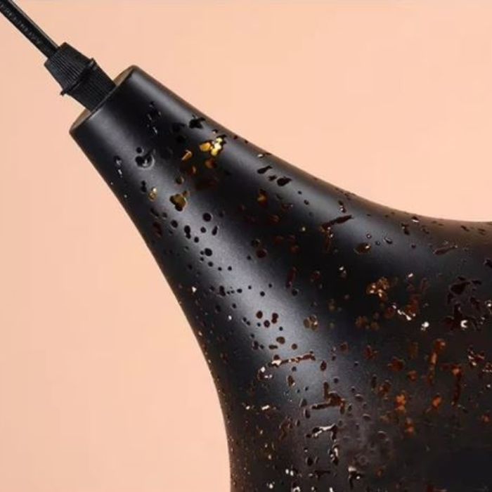 Détail du métal noir perforé d'une suspension industrielle, aux ajours lumineux évoquant une constellation étoilée.