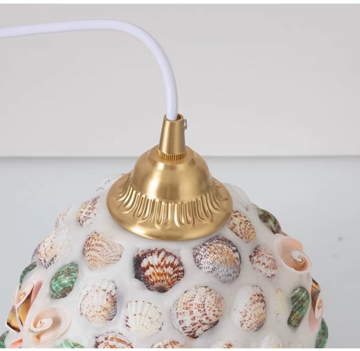 Gros plan sur la suspension en verre façonné à coquillages colorés, avec monture dorée d’inspiration rétro marine