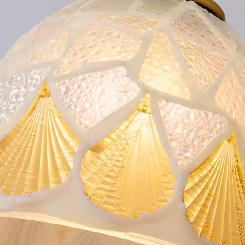 Détail d’une suspension en verre façonné aux motifs coquillage dorés, évoquant un univers marin raffiné