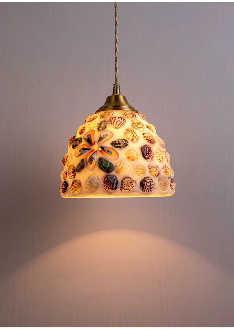 Suspension en verre façonné parsemée de coquillages colorés, diffusant une lumière chaleureuse au charme marin