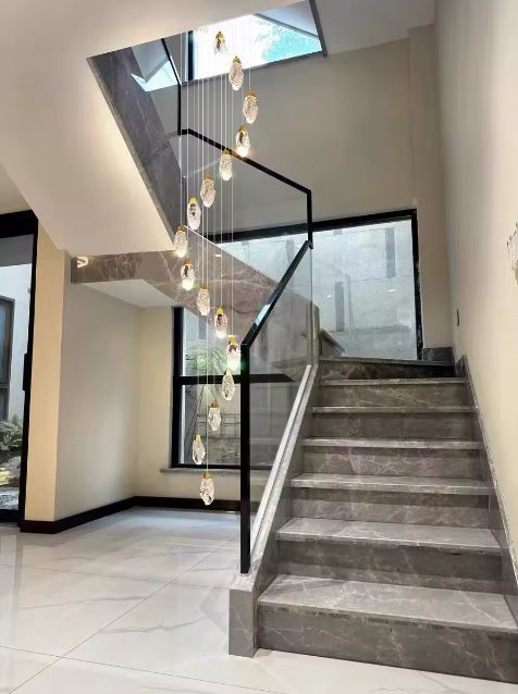 Suspension cristal en cascade dans une entrée avec escalier design, luminaire élégant aux formes inspirées de la roche naturelle.
