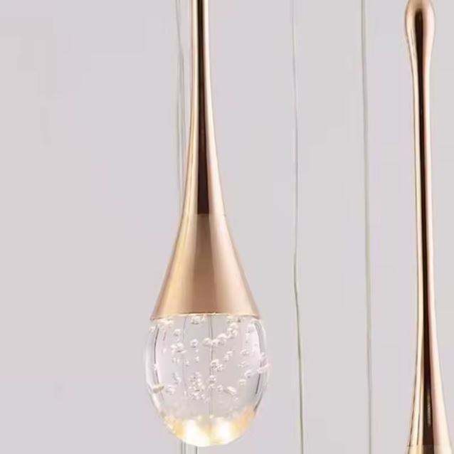 Gros plan sur une suspension cristal doré en forme de goutte, avec bulles internes pour un effet lumineux raffiné et contemporain.