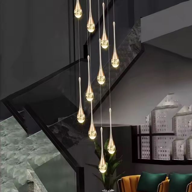Suspension cristal doré goutte à goutte, éclairant un escalier moderne avec verrière, dans un intérieur chic et contemporain.