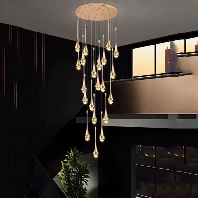 Suspension cristal doré illuminant un intérieur sombre avec élégance, idéale pour une cage d’escalier à très haut plafond ou mezzanine.