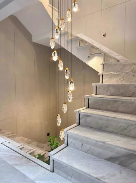 Suspension cristal pour escalier en marbre, luminaire contemporain aux pendants minéraux dans un espace à haut plafond.