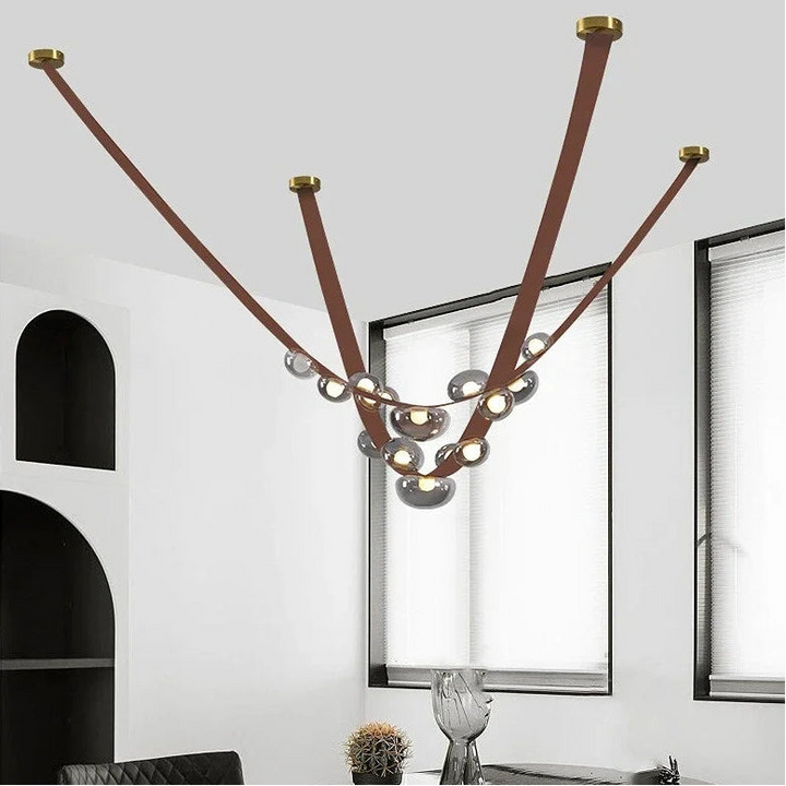 Suspension en cuir marron clair et sphères lumineuses en verre fumé apportant une touche chaleureuse et scandinave.