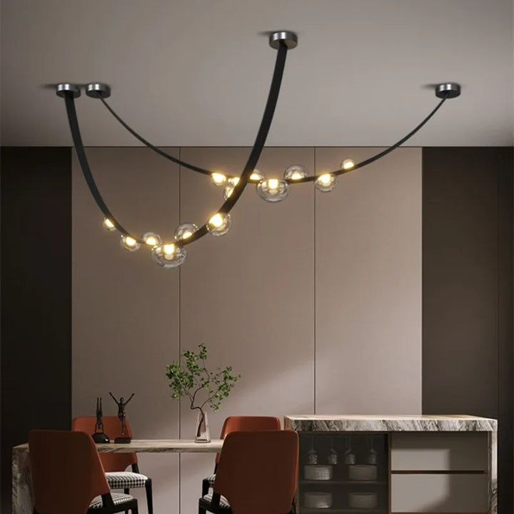 Suspension en cuir noir et sphères lumineuses transparentes mariant les tons chaleureux d'une salle à manger boisée.