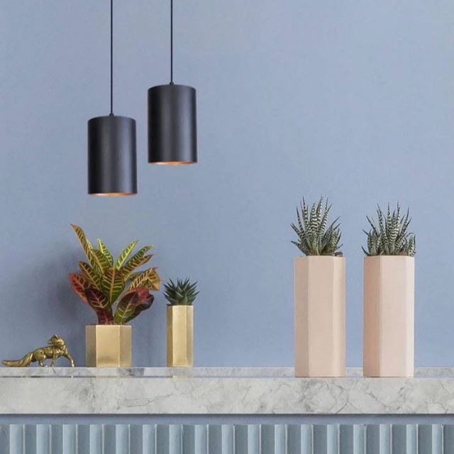 Suspension cylindrique noire élégante, mise en valeur dans un décor moderne avec des plantes et des éléments en marbre.