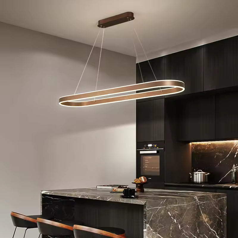 Suspension LED ovale allongée finition café, au design contemporain élégant, au-dessus d'un îlot en marbre noir.