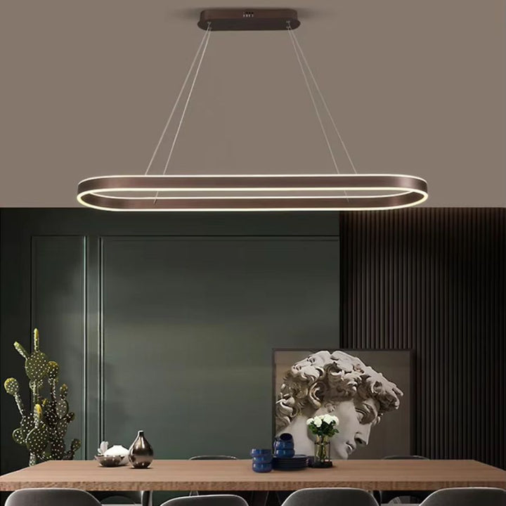 Au-dessus d'une table en bois, suspension LED à anneau ovale allongé finition café, dans une salle à manger contemporaine.