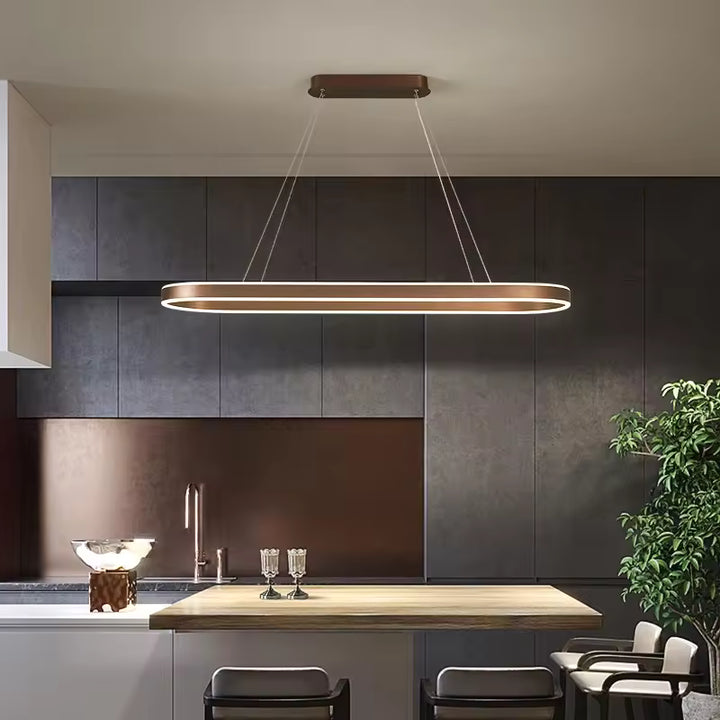 Suspension LED à anneau ovale allongé, finition café, au design minimaliste contemporain, installée au-dessus d'un îlot de cuisine.