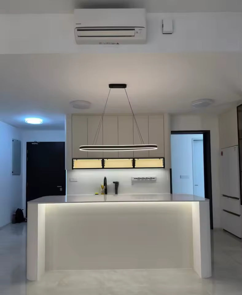 Vue frontale d'une suspension LED noire à anneau ovale allongé, au style minimaliste, éclairant un îlot de cuisine blanc.