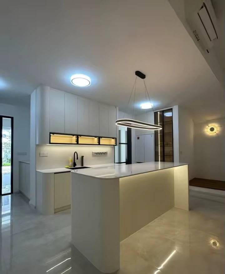 Une suspension LED noire à anneau ovale allongé surplombe un îlot de cuisine blanc, dans un intérieur moderne et épuré.