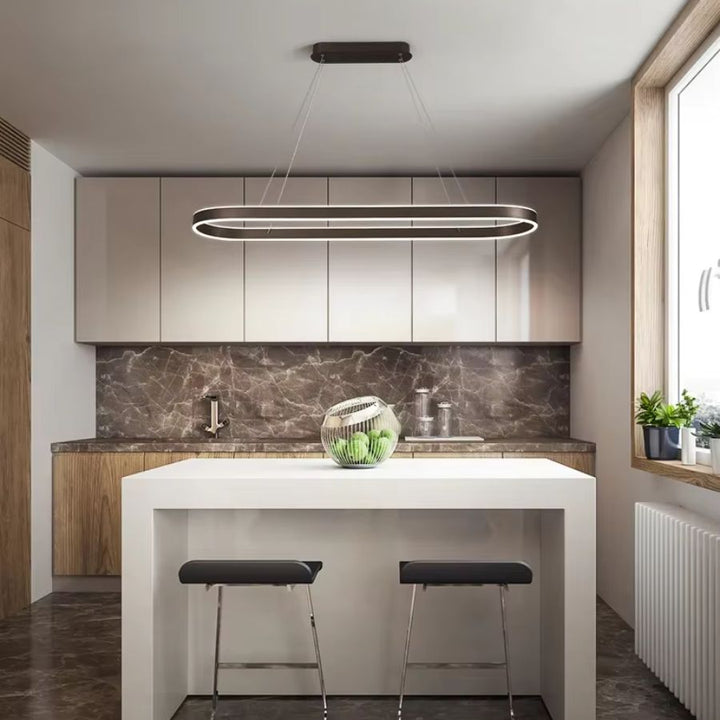 Au-dessus d'un îlot blanc, suspension LED noire à anneau ovale allongé, dans une cuisine moderne au style minimaliste.