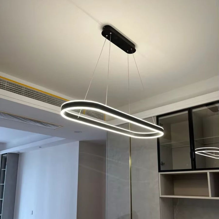 Vue en contre-plongée d'une suspension noire à anneau ovale allongé, aux lignes futuristes et à l'éclairage LED intégré.