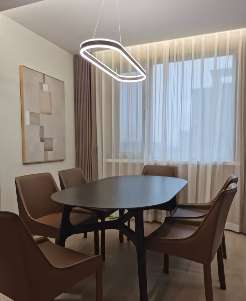 Au-dessus d'une table noire, suspension LED à anneau ovale allongé au design minimaliste, dans une salle à manger élégante.