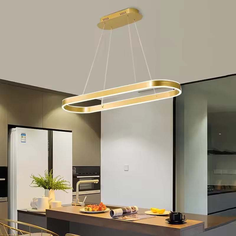 Au-dessus d'un îlot de cuisine moderne, suspension dorée à anneau ovale allongé, au design épuré et contemporain.